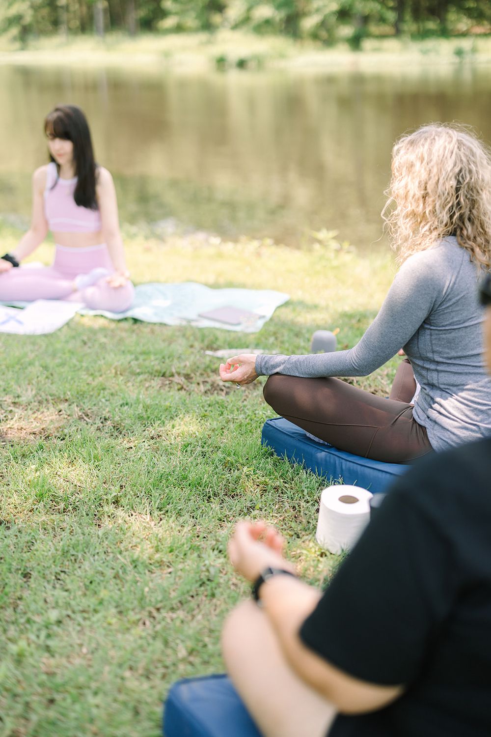 People relax on grassy lawn near a calm lake during a peaceful outdoor gathering.