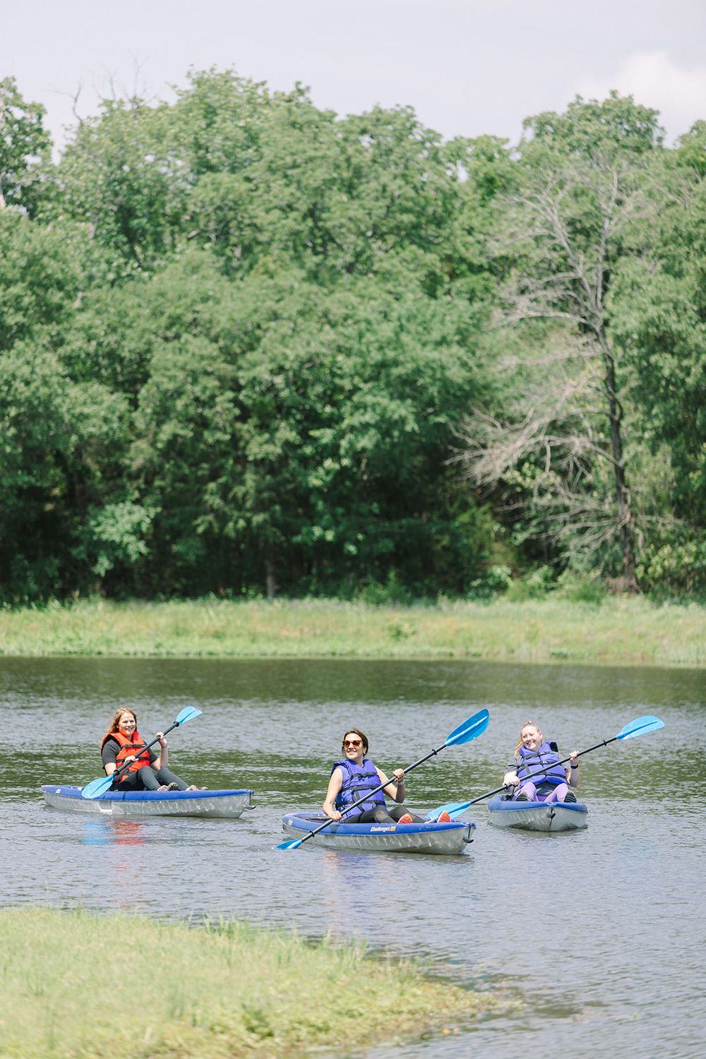 A group of kayakers paddling across a tranquil lake surrounded by lush green trees.