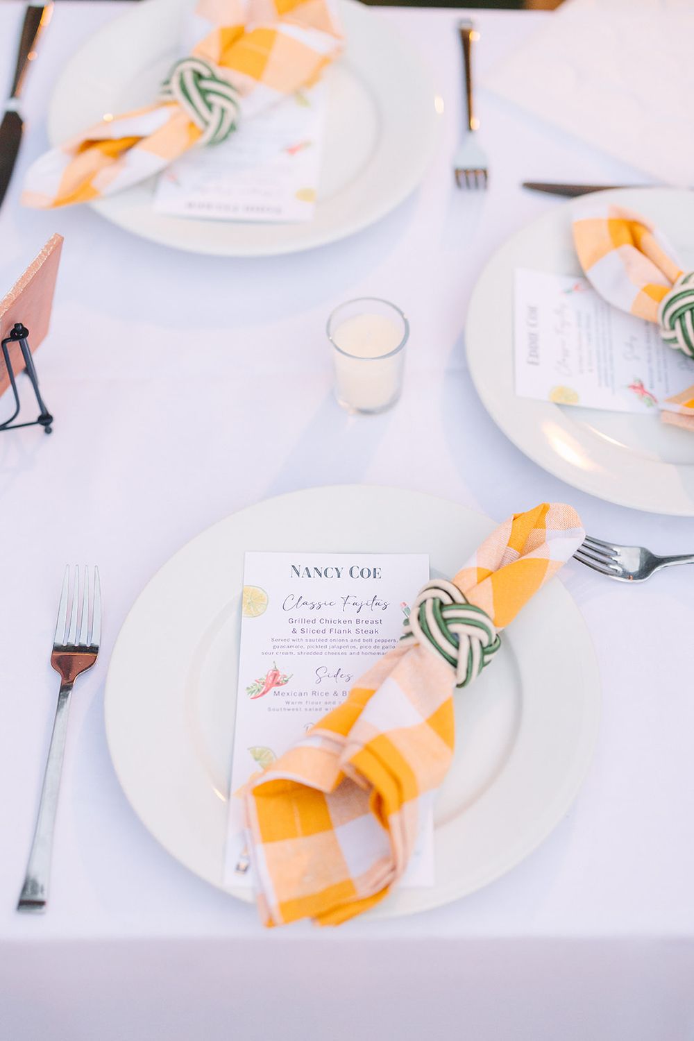 Elegant place settings with white plates, peach napkins, nautical knot napkin holders and menu cards on a white tablecloth.