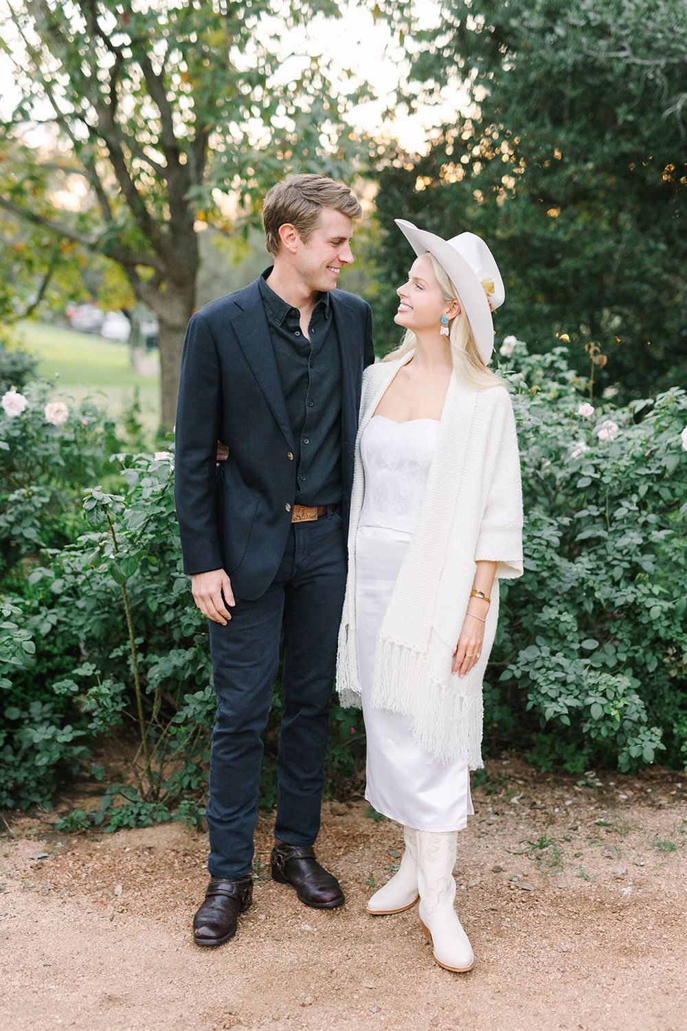 Two people in white and dark attire sharing a moment together in a garden setting.