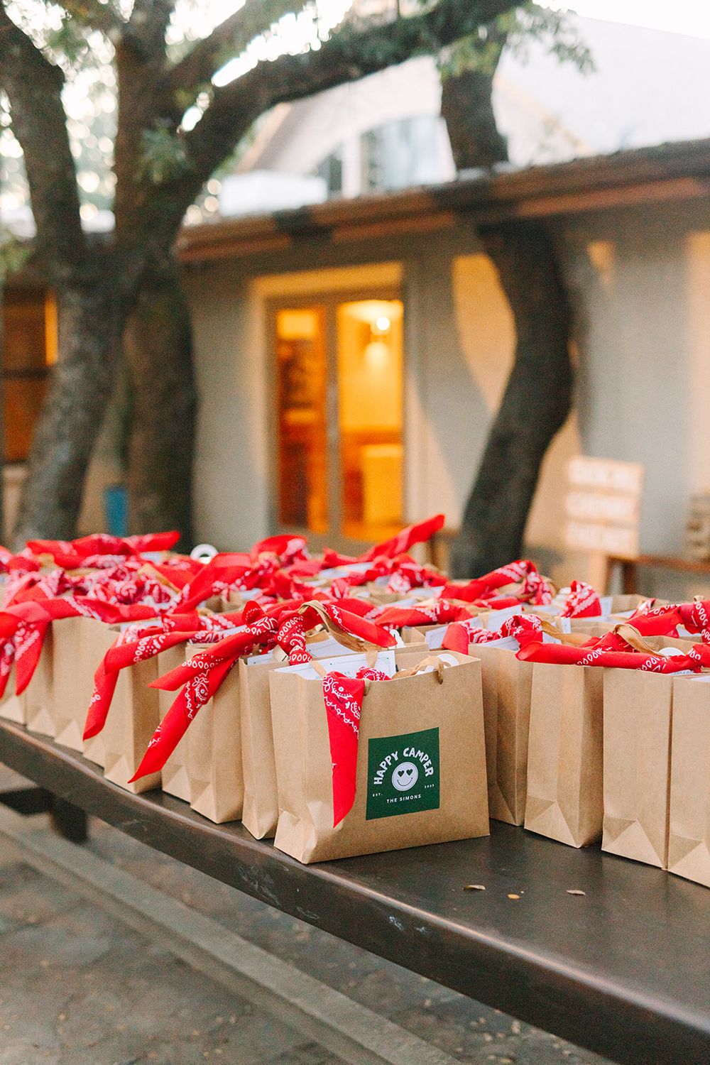Brown paper gift bags with red ribbons and green tags arranged in a row on outdoor wooden benches.