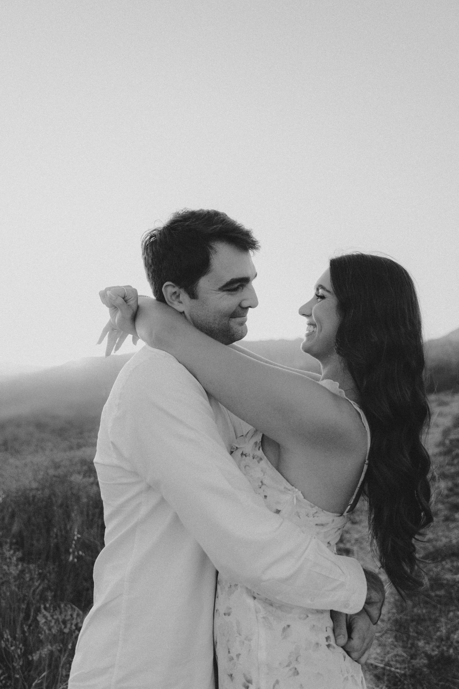 A romantic couple in white clothing embraces in a field, shown in a series of candid black and white photographs.