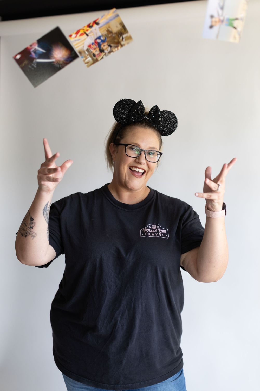 Person wearing Mickey Mouse ears and black t-shirt makes peace signs while posing against white wall.