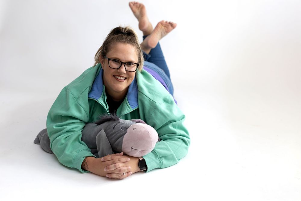 A person wearing a mint green jacket and glasses lies comfortably on their side in a relaxed pose.