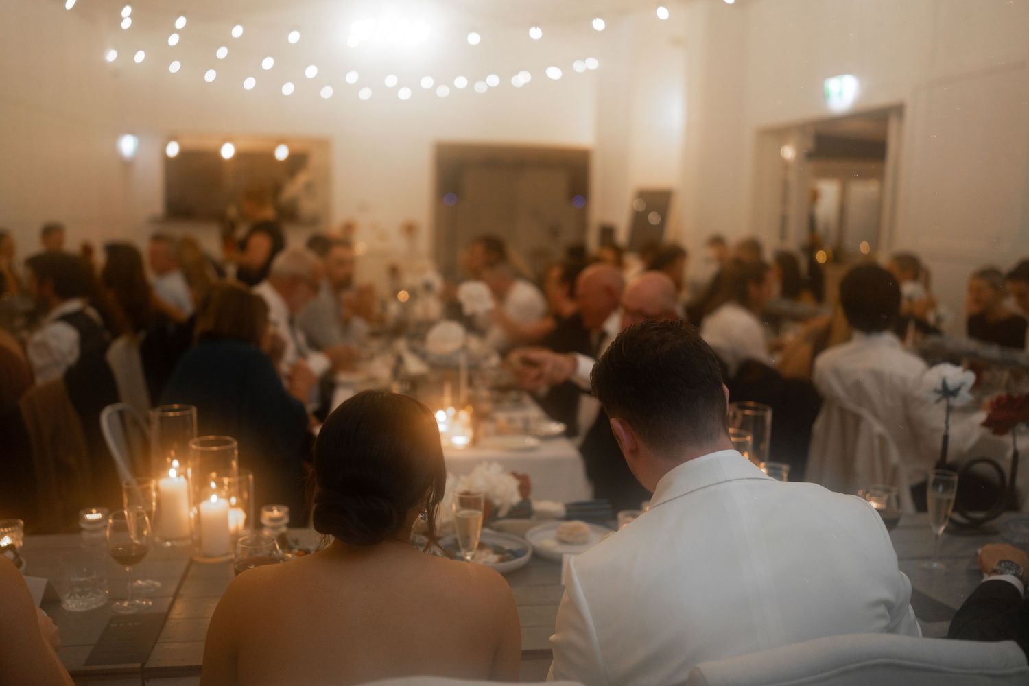 Guests gather at candlelit reception tables under ambient string lights creating an intimate wedding atmosphere.