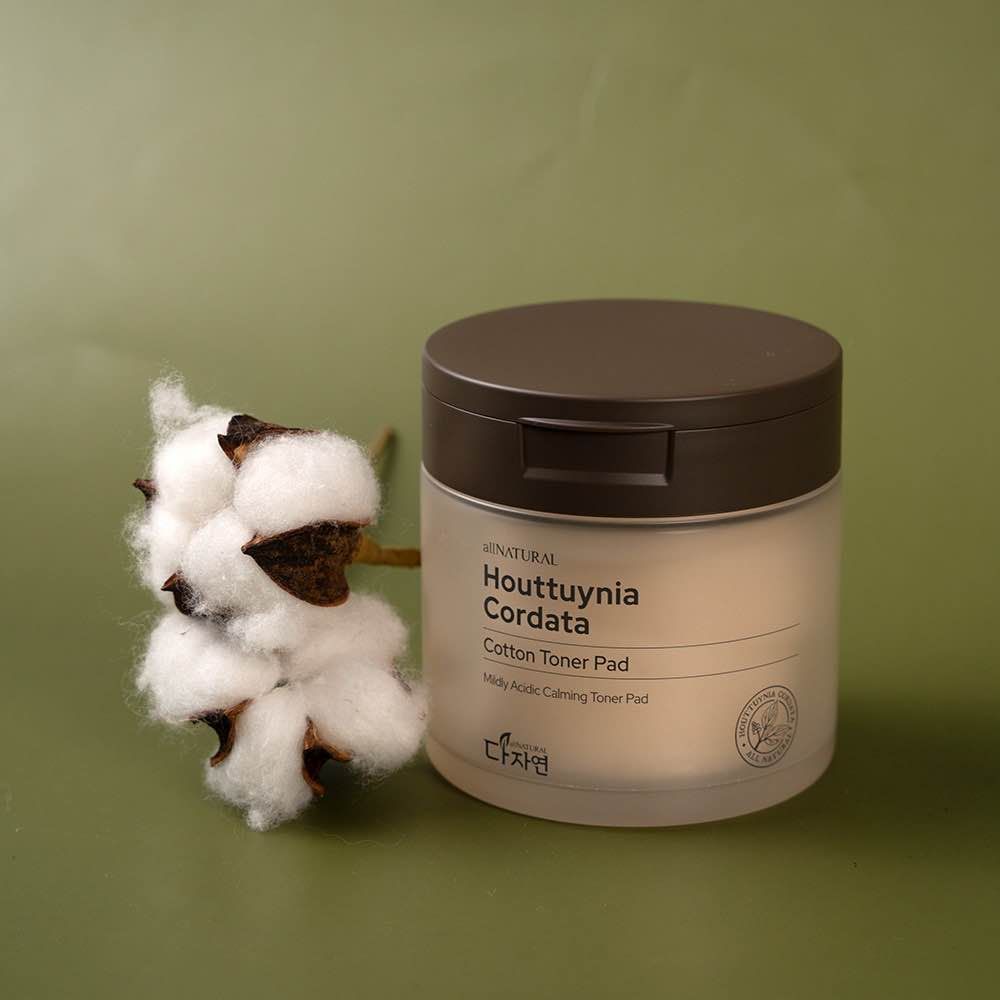 Skincare cream jar with cotton plant branch displayed on green background.