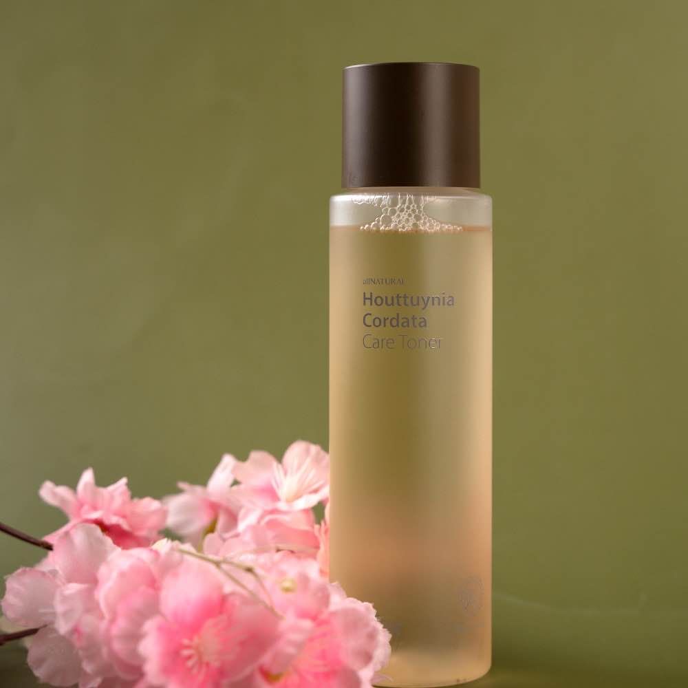 Glass bottle of skincare toner with pink flowers against green background.