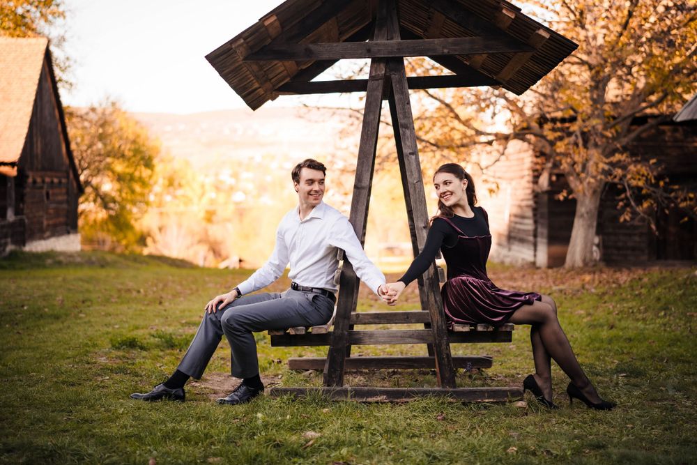 Romantic autumn engagement photos under wooden gazebo during golden hour.