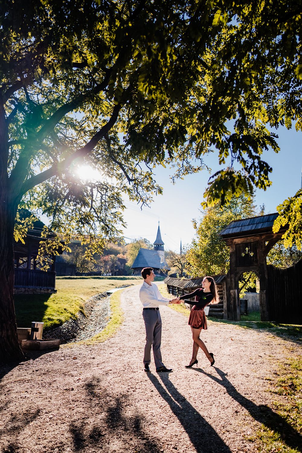 Couple walking along sunlit path with trees casting dramatic shadows.