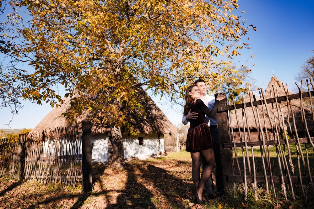 Autumn engagement session with rustic wooden fence and golden foliage.