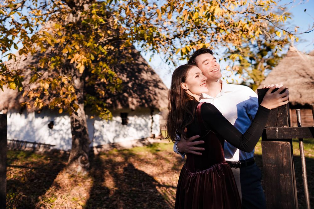 Romantic couple poses beneath fall trees with golden leaves.