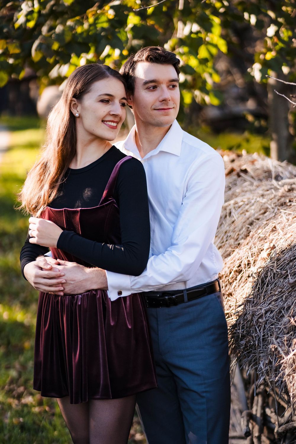 Couple embracing outdoors wearing coordinated formal attire against natural backdrop.