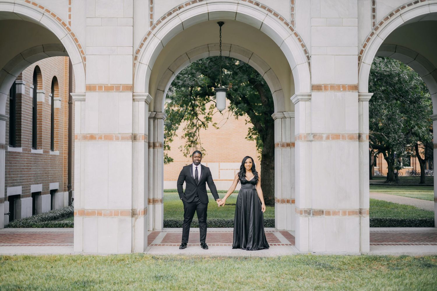 Two people in formal attire stand under white stone arches at a historic building entrance.