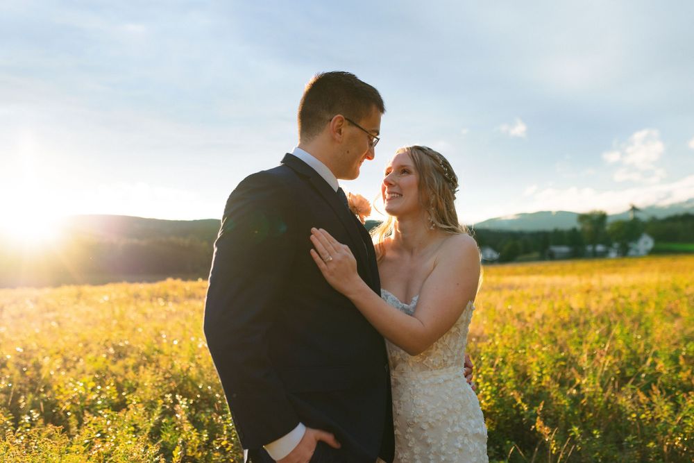 A couple embraces in a sunlit yellow flower field with rolling hills in the background during golden hour.