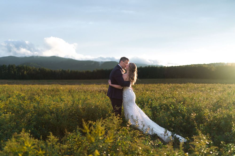 A couple embraces in a scenic mountain meadow filled with yellow wildflowers at sunset.