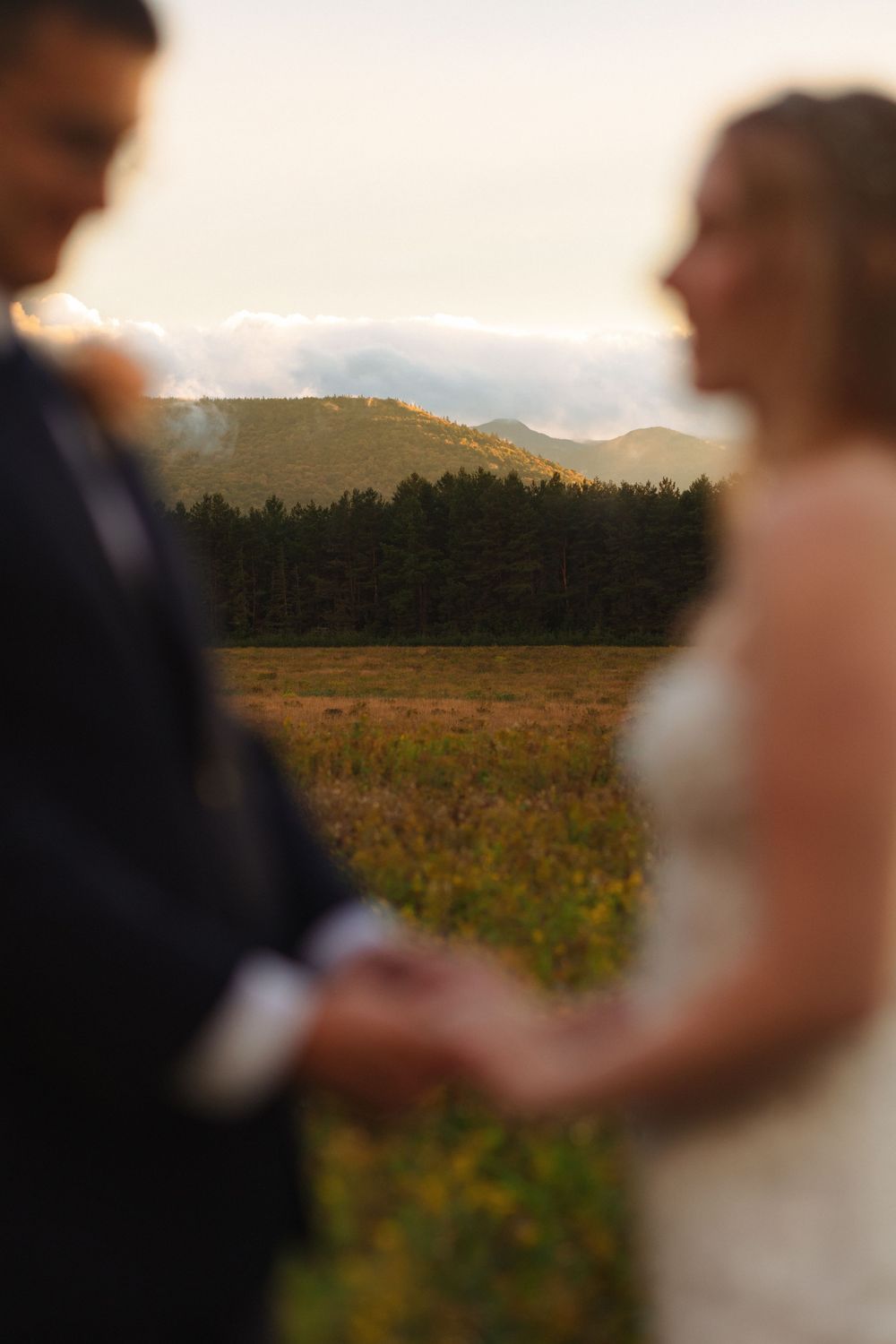 A soft-focus wedding ceremony moment silhouetted against a scenic mountain landscape with golden fields at sunset.