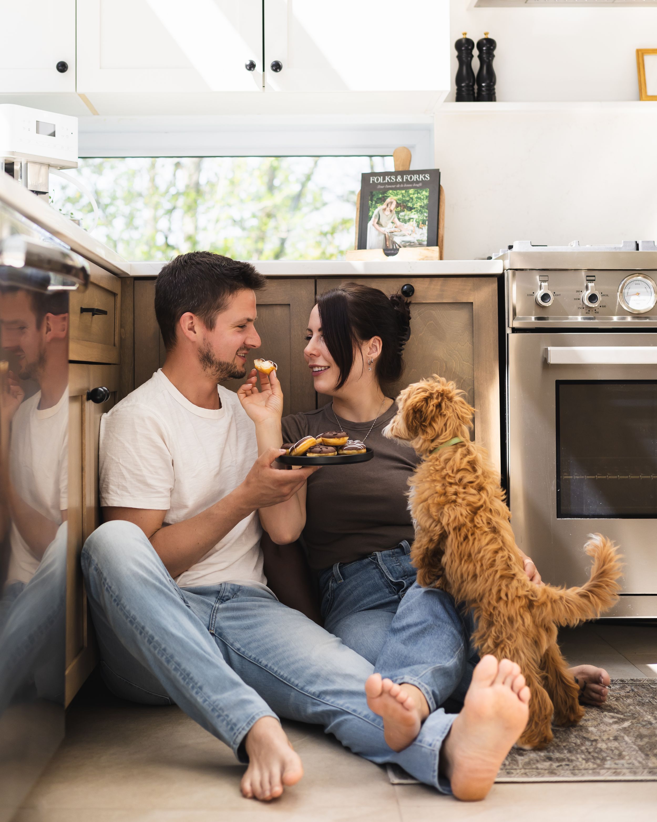 A couple enjoying snacks on the kitchen floor with their golden dog.