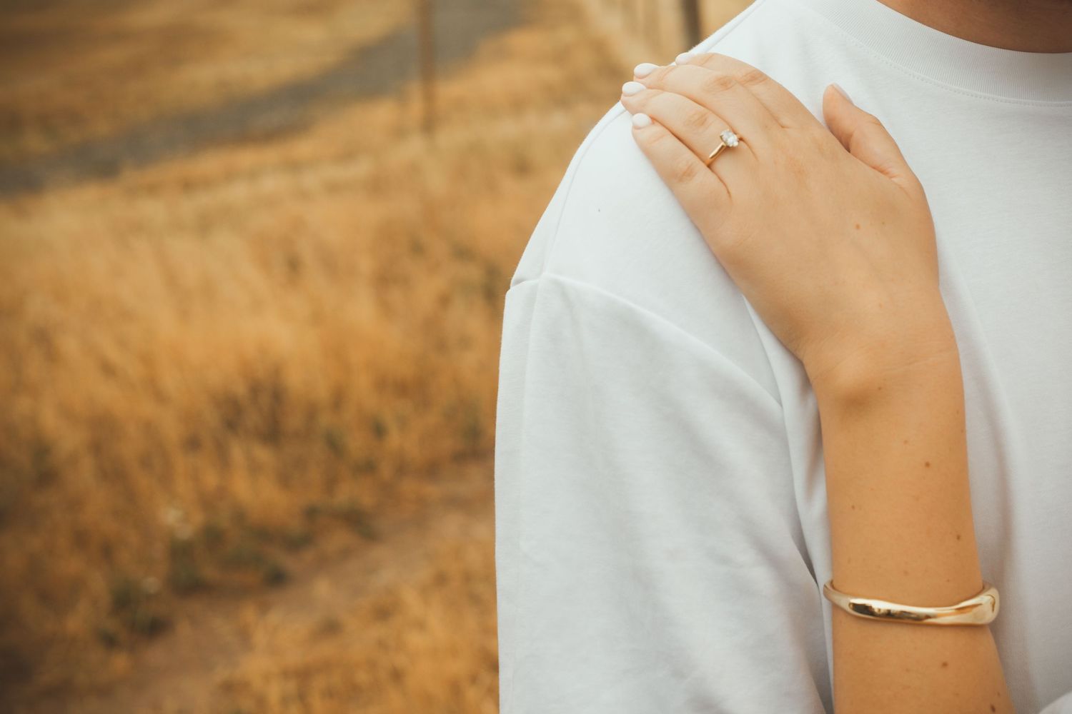 Close-up of a hand wearing an engagement ring resting on a white-clothed shoulder.