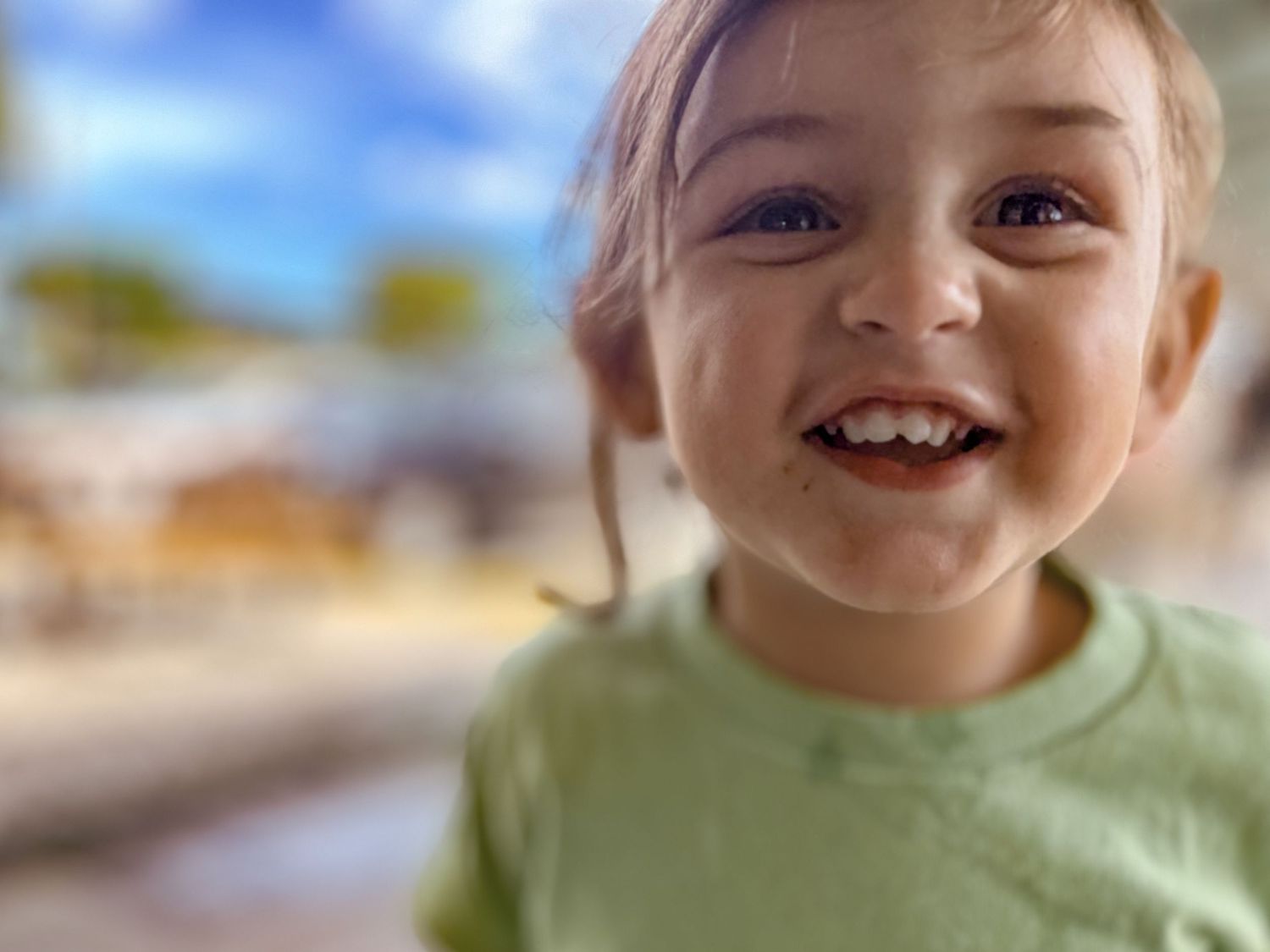 A close-up portrait showing joy and excitement against a blurred outdoor background.