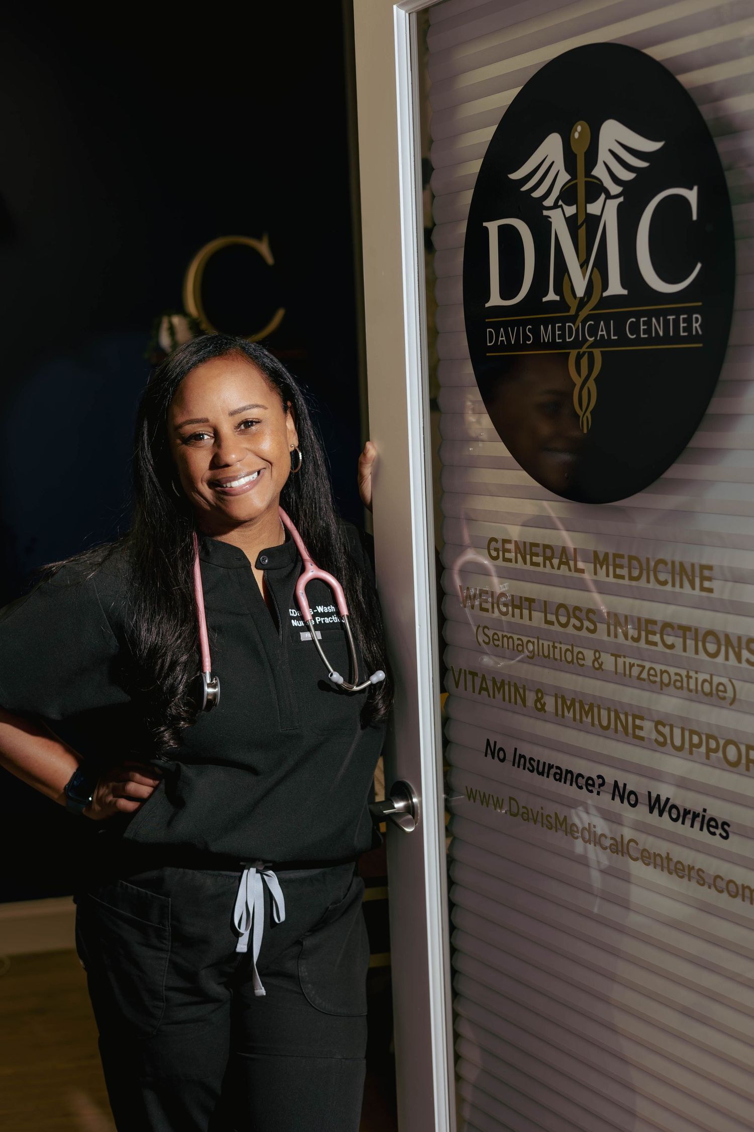 A female medical professional in scrubs poses beside a Davis Medical Center office door sign.