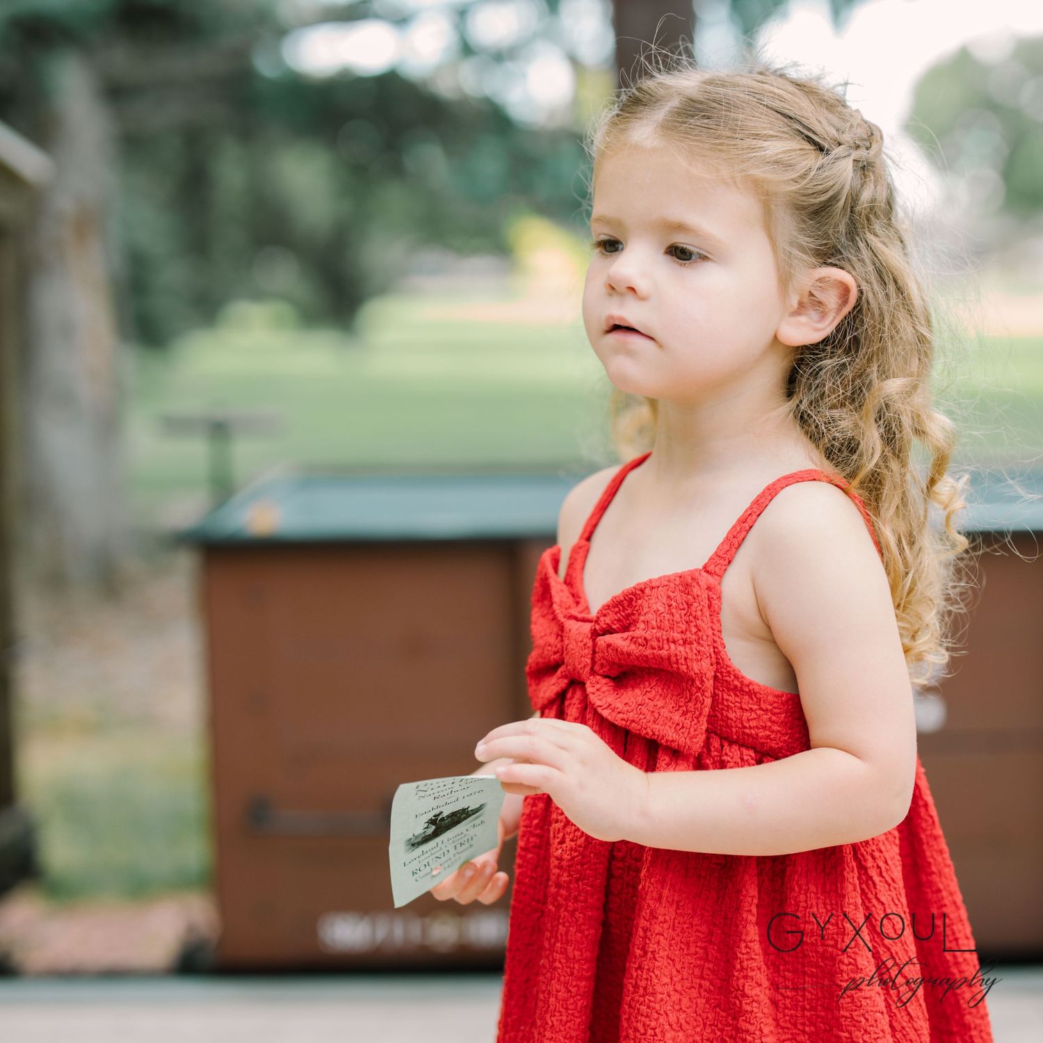 Young child in a red sleeveless dress standing on a wooden deck.