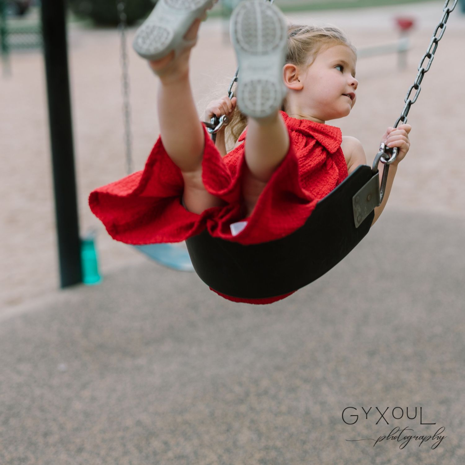 A child in a flowing red dress swings joyfully at a playground.