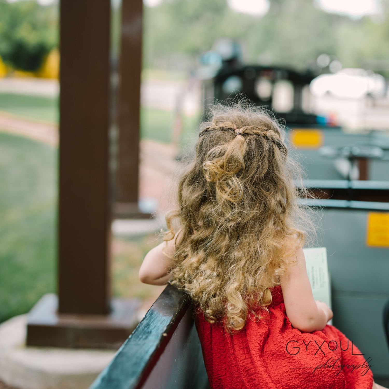 Back view of a child in a red dress looking over a railing outdoors.