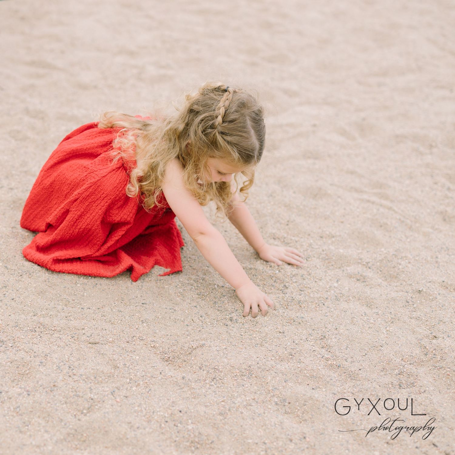 A child in a red dress explores the ground in an outdoor play area.