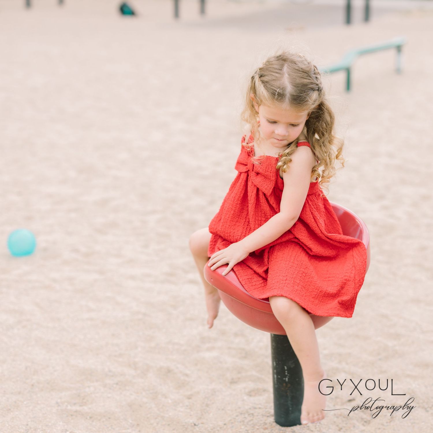 A child in a red dress plays and twirls on a playground.