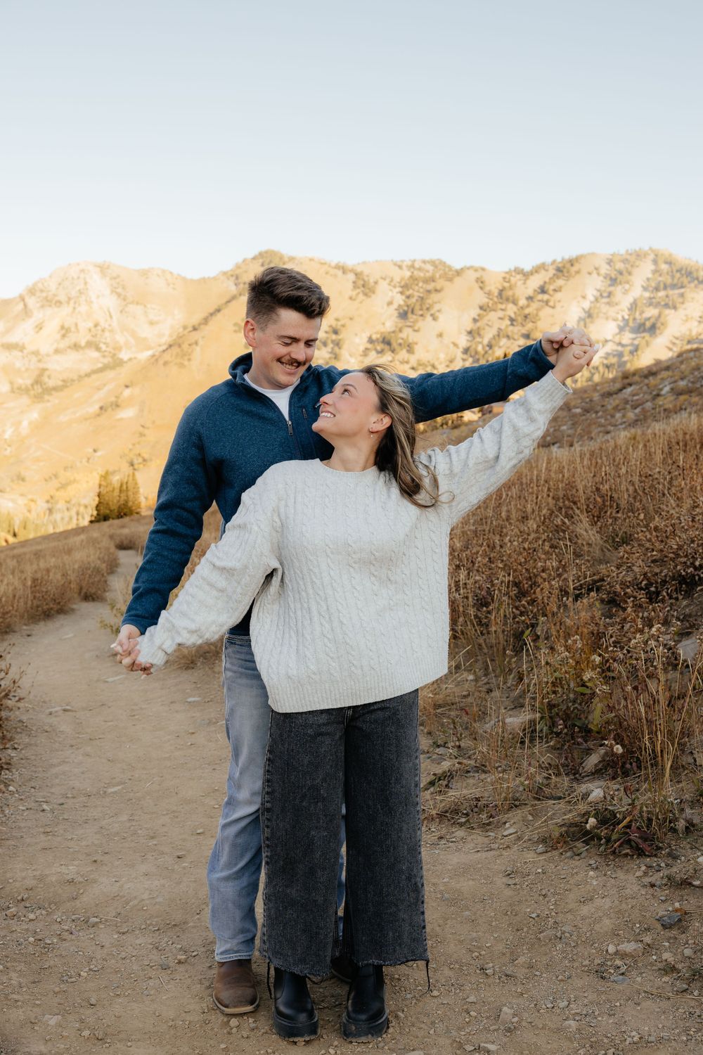 Couple embracing on mountain trail at sunset, woman pointing at the sky.