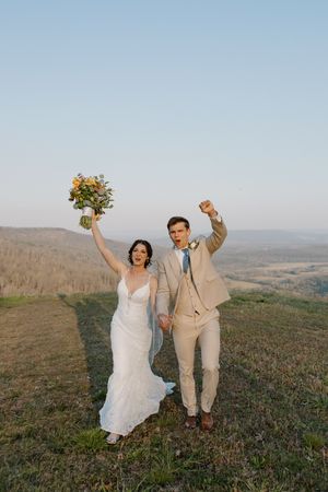 A couple celebrates their wedding day on a hilltop meadow with sweeping mountain views in the background.