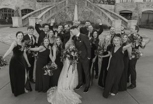 A black and white wedding party photo showing a formal group gathered on elegant stone steps in classic formal attire.