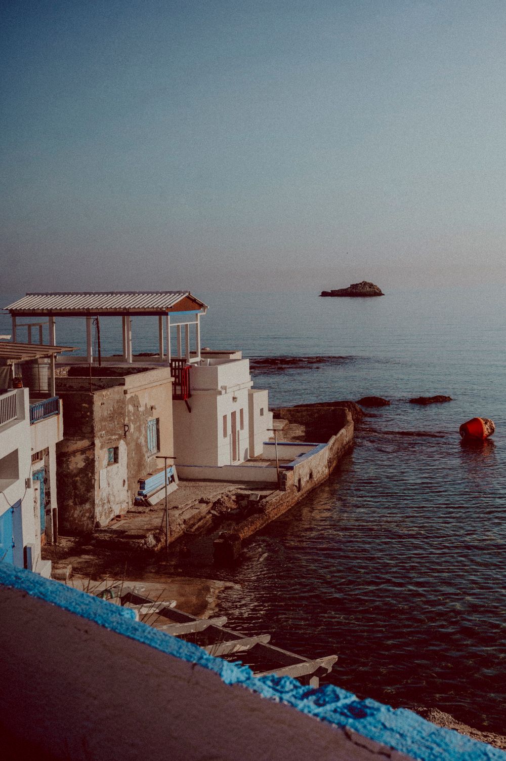 Coastal Mediterranean building with covered terrace overlooking blue ocean and distant island.