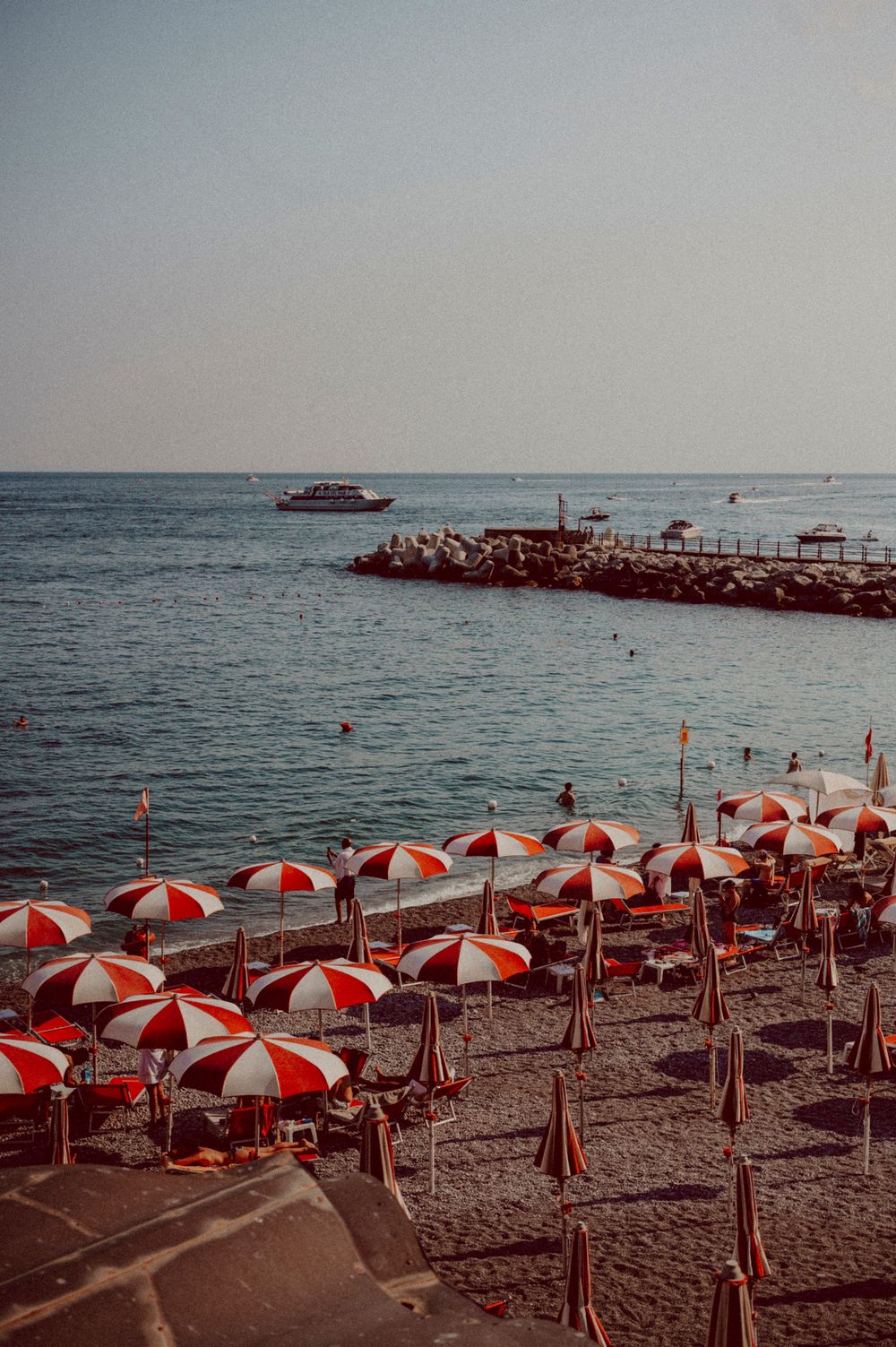 Red and white striped beach umbrellas lined up along a rocky Mediterranean coastline.