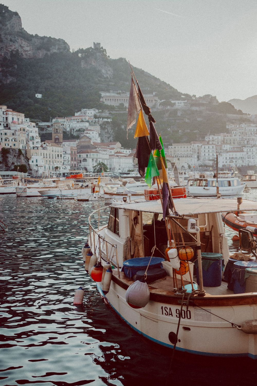 Traditional fishing boat with colorful flags docked in harbor with white coastal buildings in background.