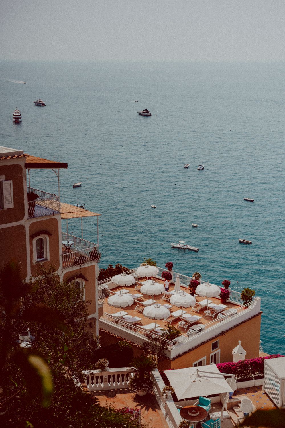 Aerial view of a seaside terrace with white umbrellas overlooking blue Mediterranean waters.