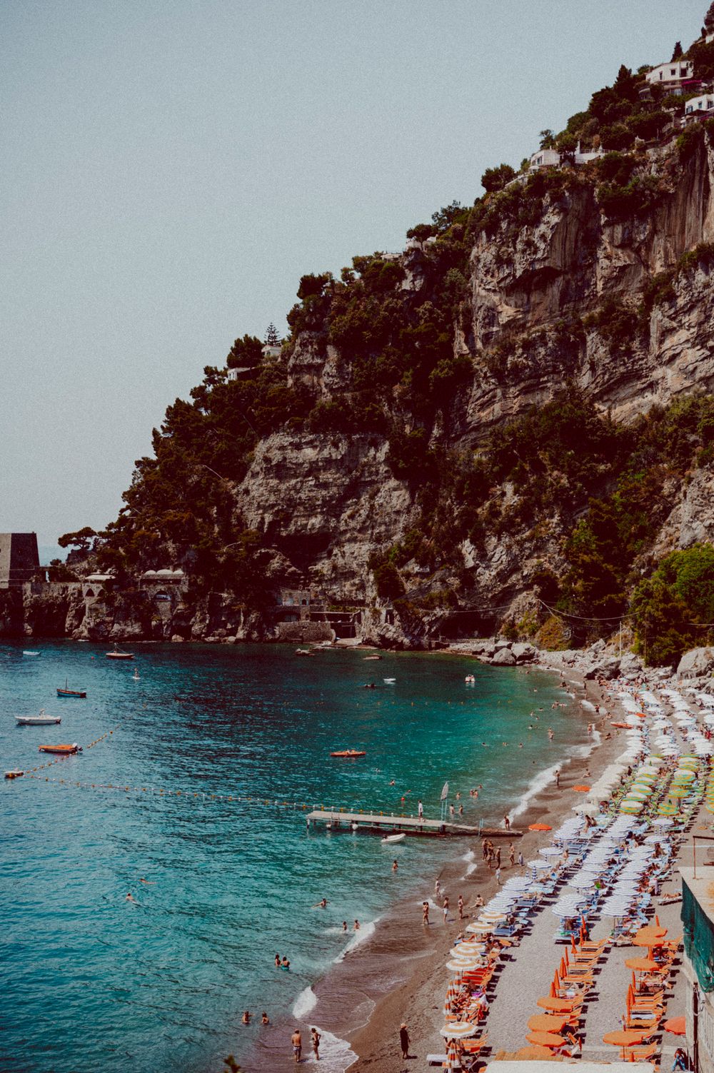 Scenic Mediterranean beach cove with orange umbrellas and sunbathers nestled between dramatic rocky cliffs.