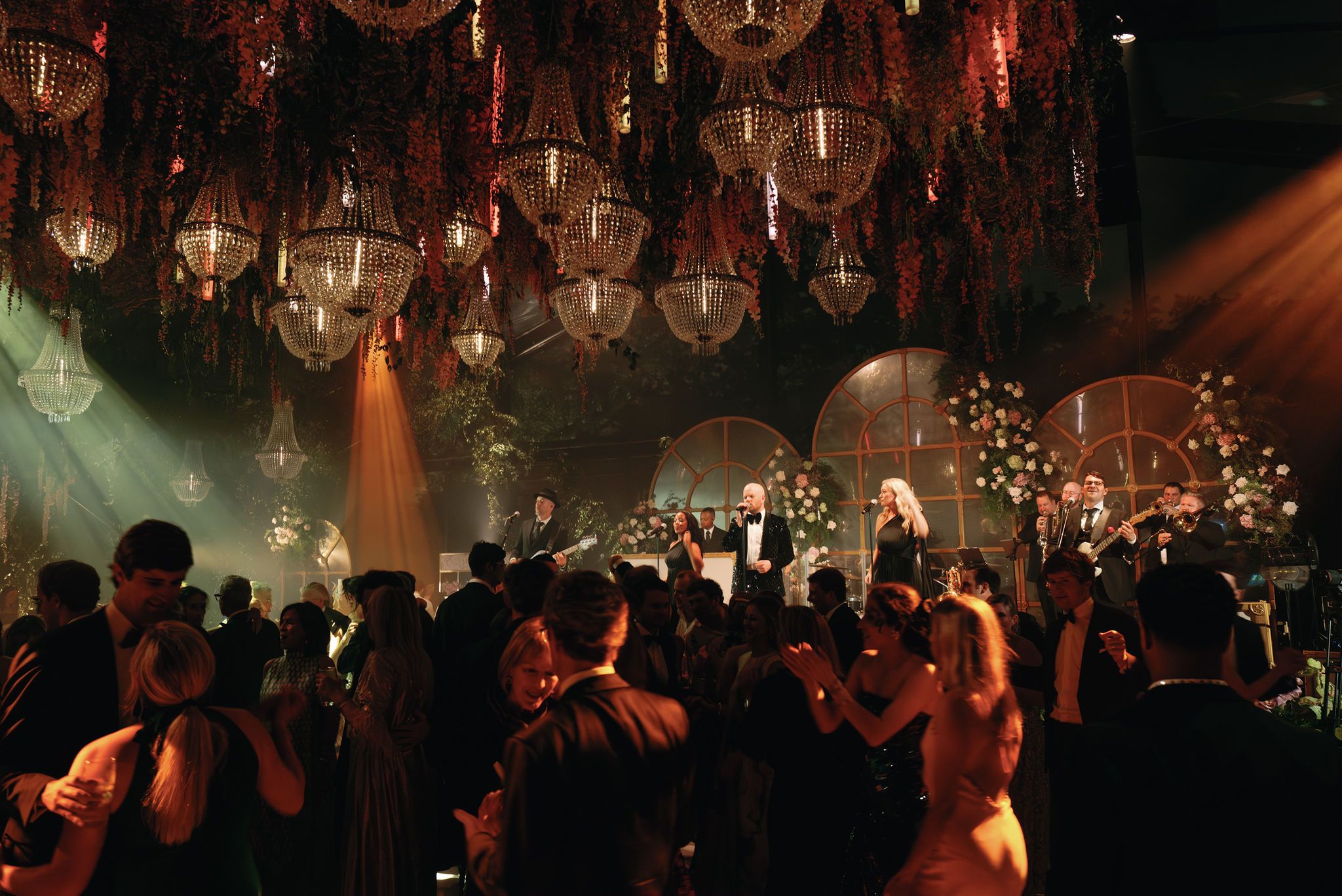 A crowded nightclub dance floor illuminated by hanging glass orbs and colorful spotlights creating a moody atmosphere.