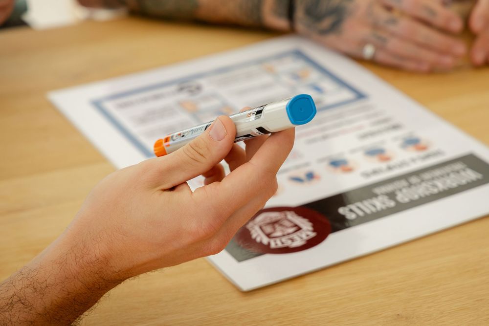 Hand holding an EPIPEN over a document on how to administer epinephrin injections, first aid training Mesh Education stock images