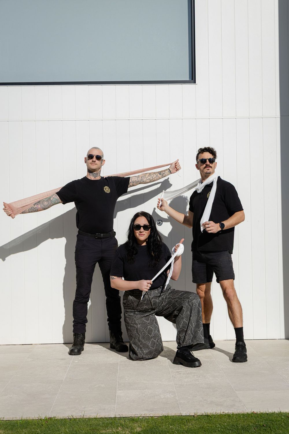 Three people in black clothing pose together against a white wall, Mesh Education Branding photoshoot