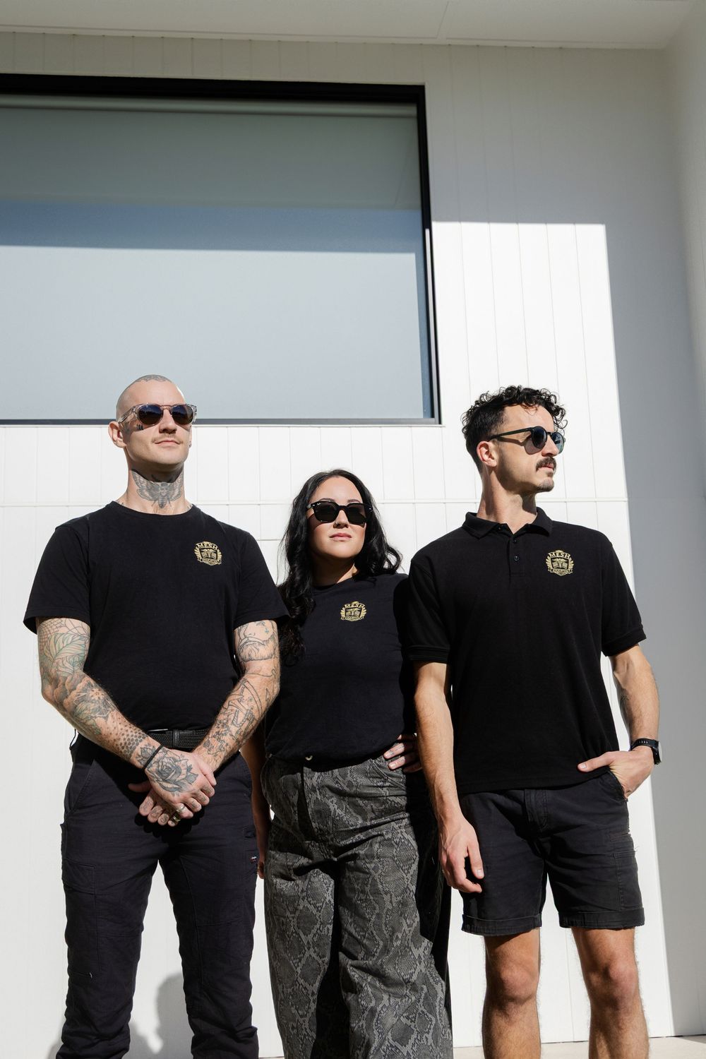 A group of people wearing black uniform and sunglasses stand together against a white wall. mesh Education branding photography