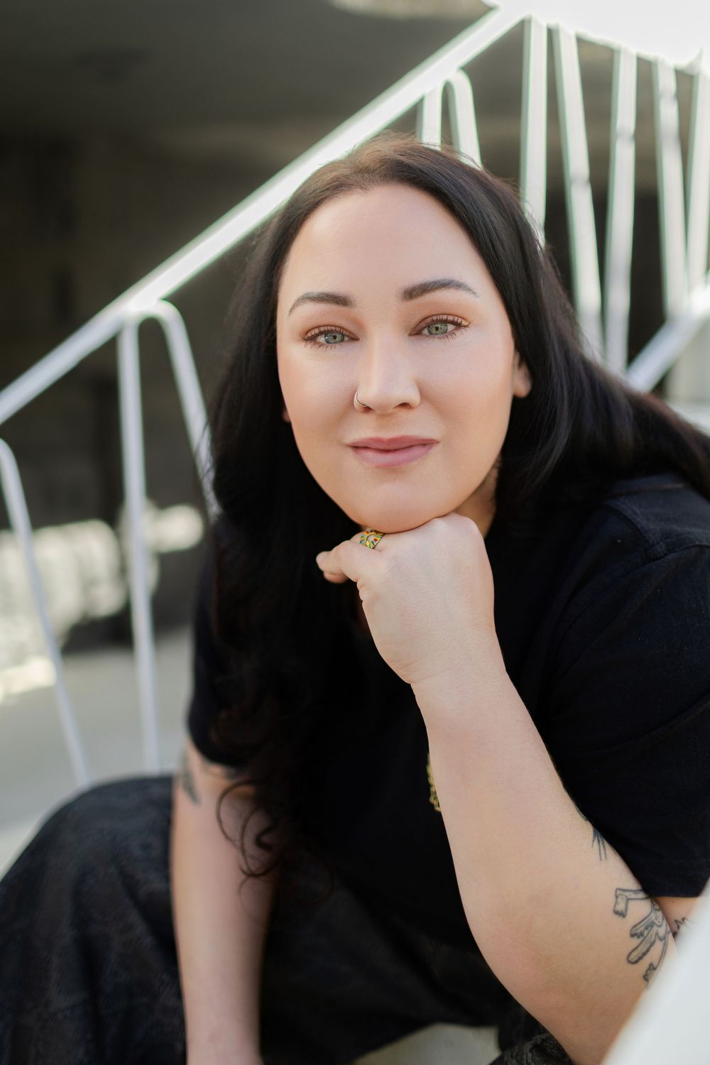Portrait of someone with long dark hair resting their chin on their hand near white stairs outdoors. Contemporary corporate photography