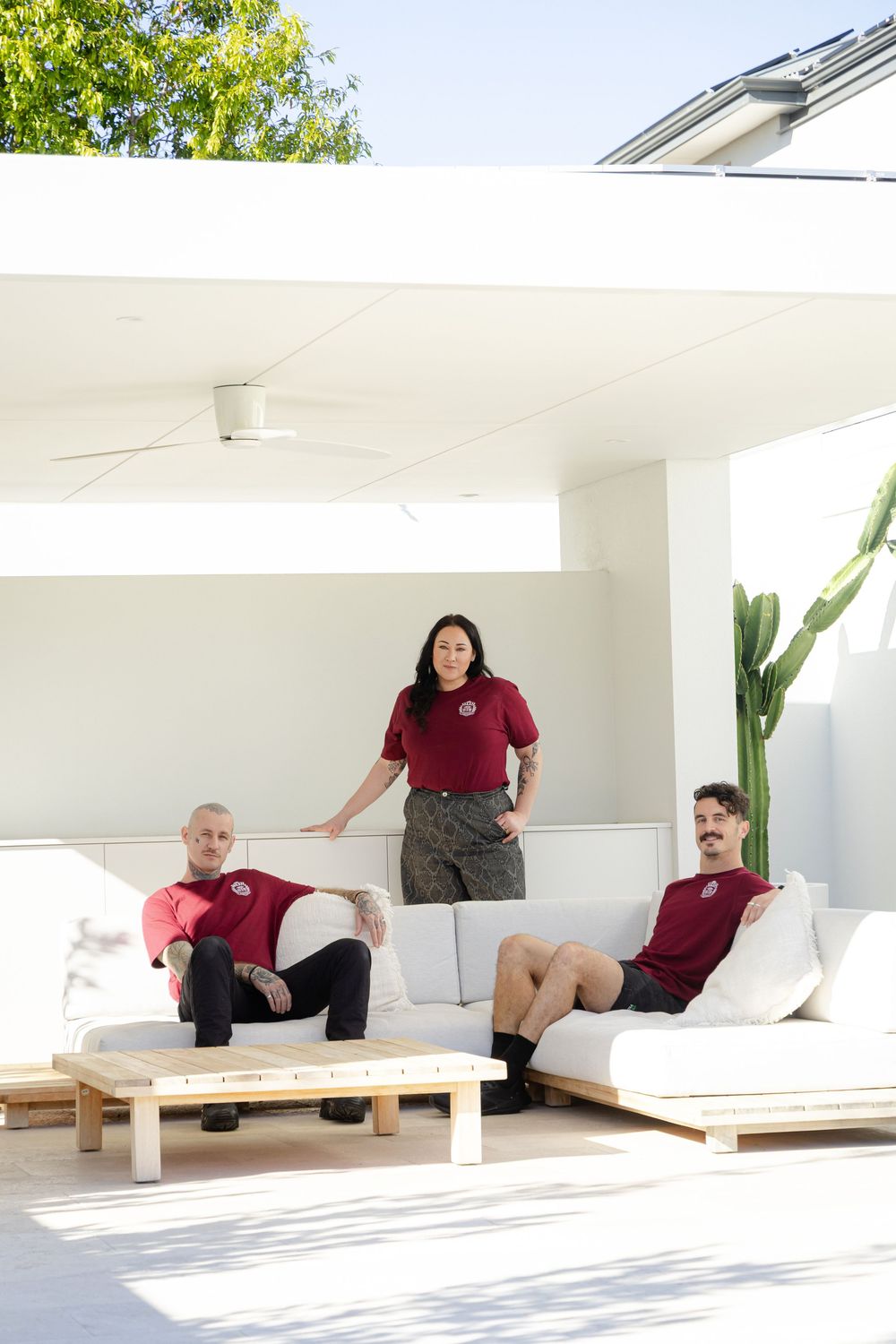 team portraits, three people in matching burgundy shirts relax on white outdoor patio furniture in a modern space. Munroe poolhouse