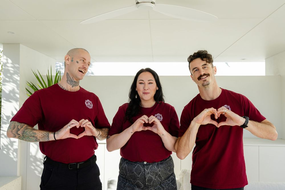 Three people wearing red shirts stand together making heart shapes with their hands while smiling. fremantle branding photography