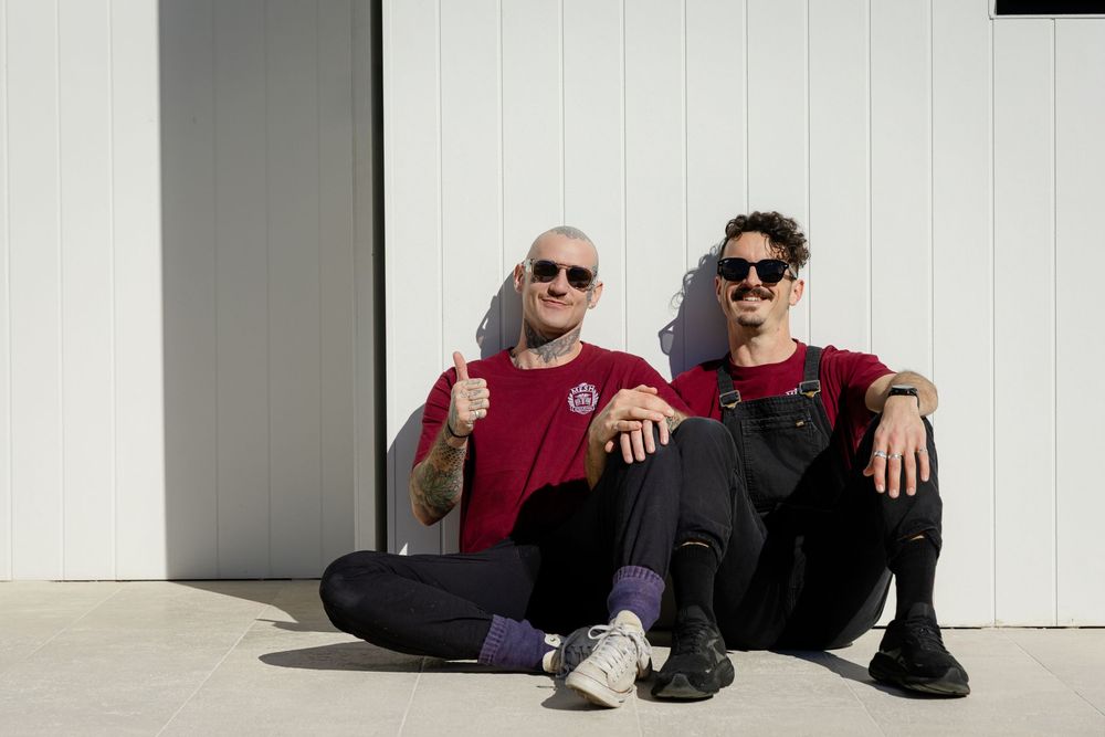 Two people in red and black casual wear sitting together against a white wall in sunlight.