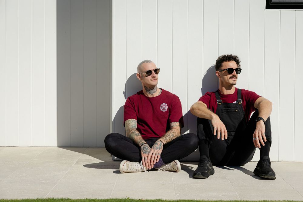 Two people in burgundy shirts and dark pants sit casually on a white ledge outdoors. trending branding photography