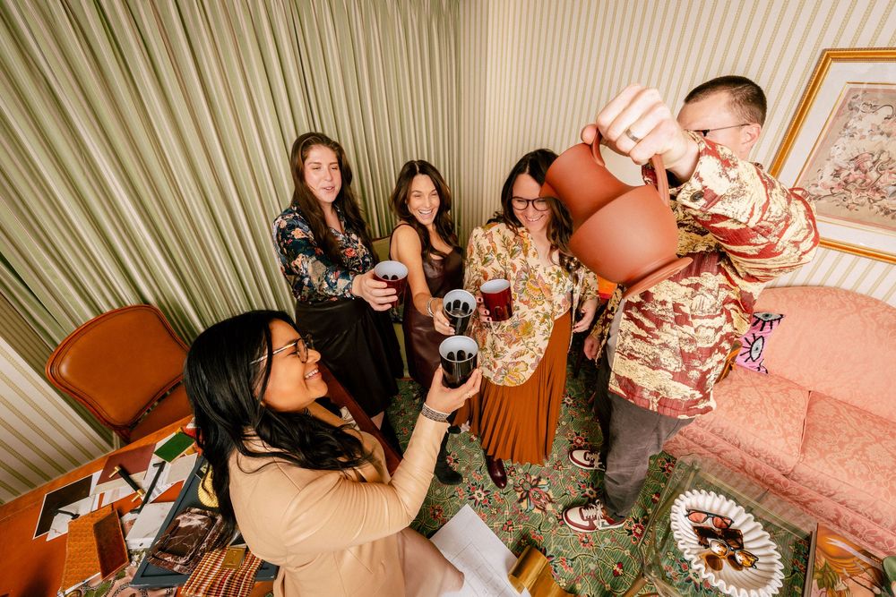 Group of friends gathering in a retro-styled room with orange furniture toasting and having drinks together.
