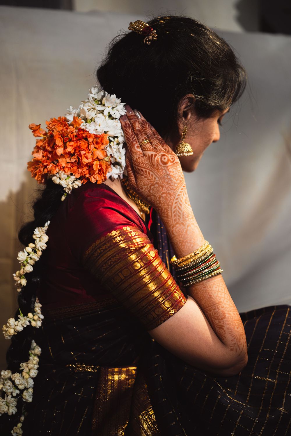 Traditional Indian bride in red sari with intricate henna designs and fresh floral hair decorations in orange and white.