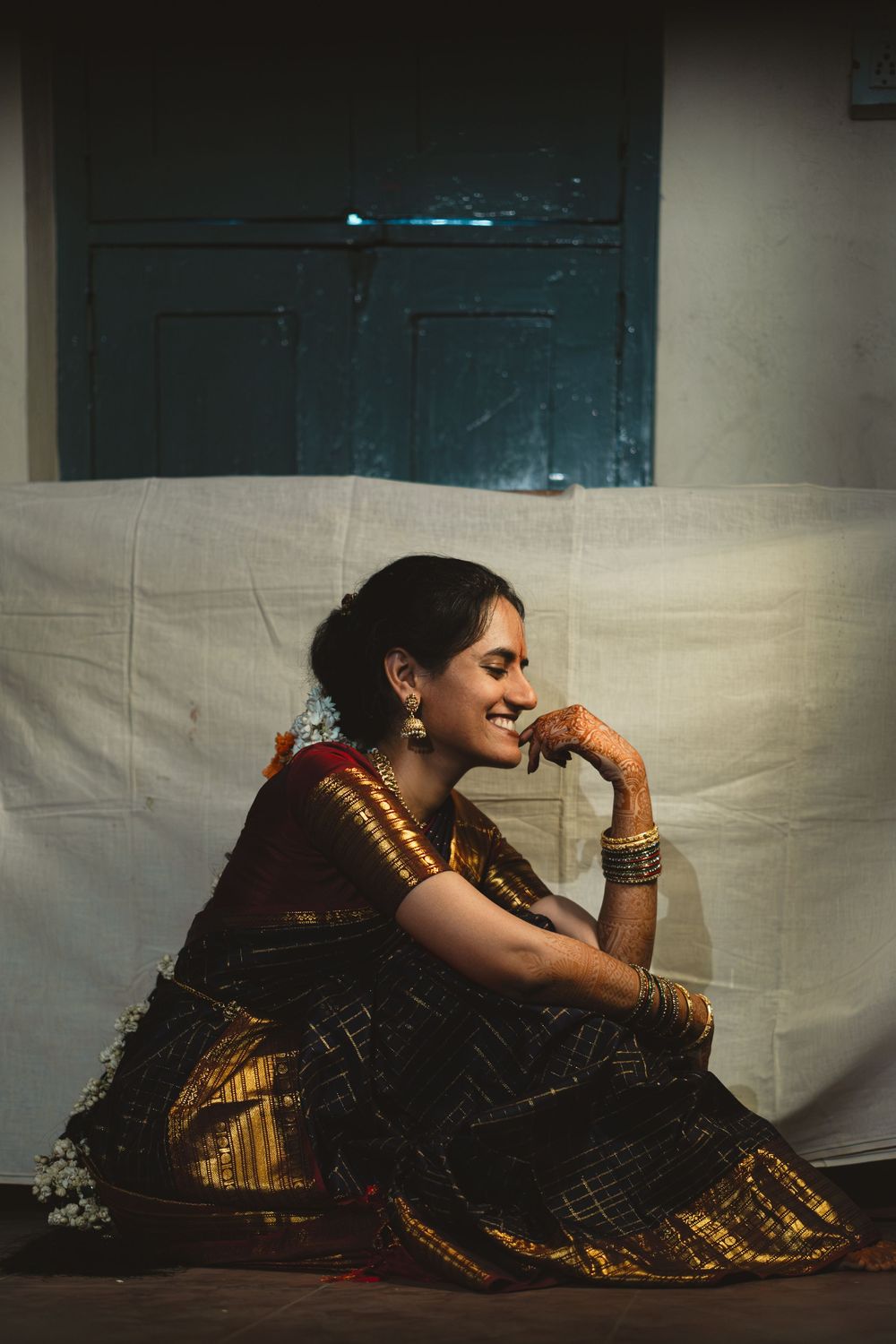 A figure in a traditional black and gold Indian sari poses gracefully in a reclining position against a light backdrop.