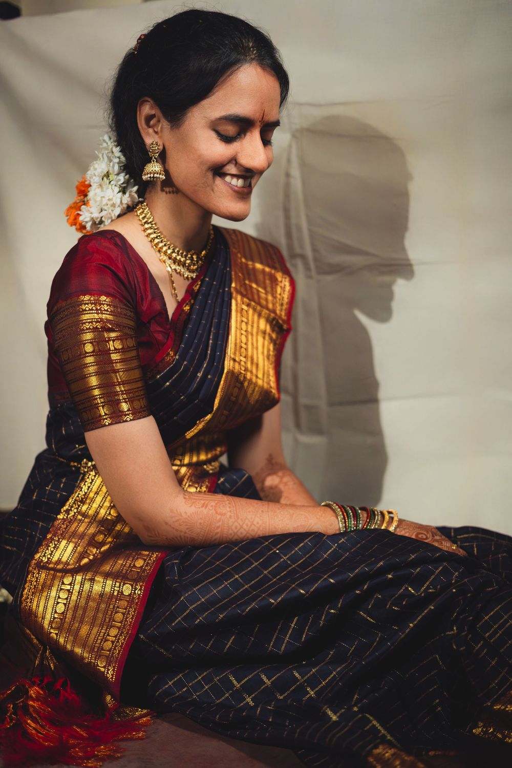 Traditional Indian classical dancer wearing a maroon and navy silk saree adorned with gold jewelry and flowers in her hair.